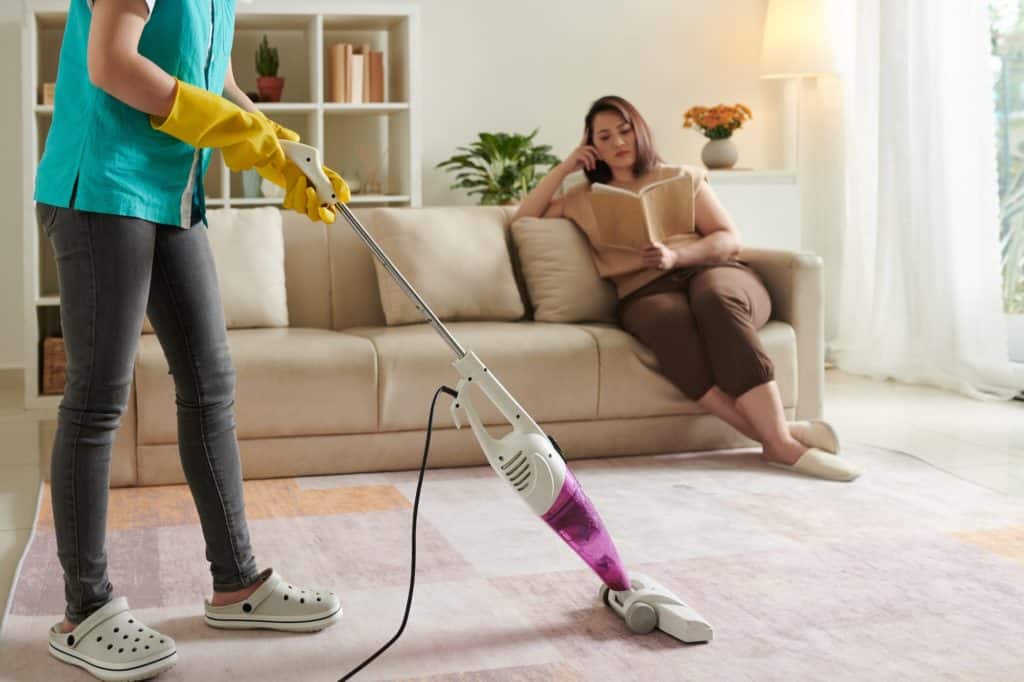 Female janitor with vacuum cleaner in room