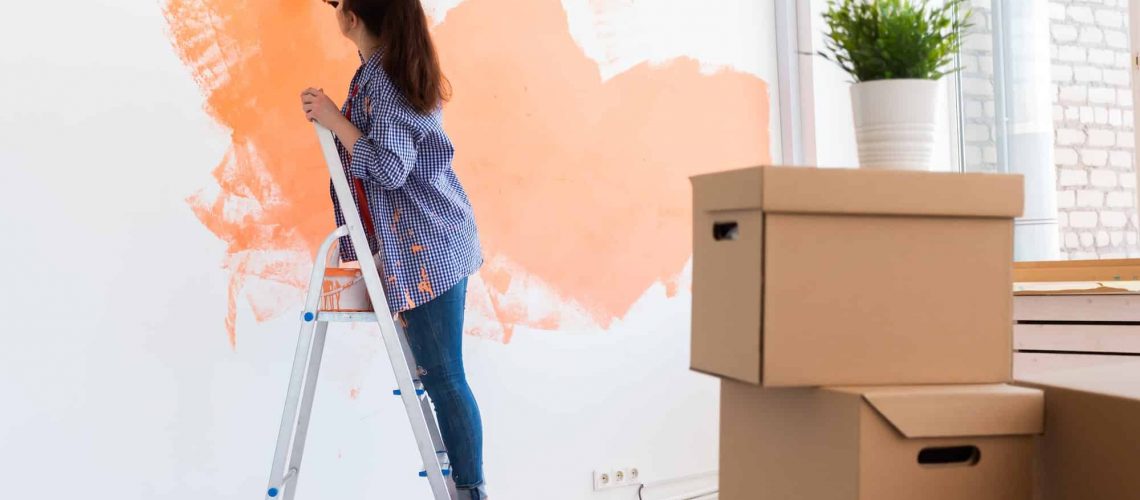 Cheerful woman painting the walls of new home. Renovation, repair and redecoration concept